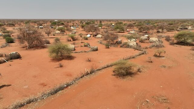 Aerial view of traditional dwellings scattered across the arid landscape with sparse trees and red earth in Wajir, Wajir County, Kenya.