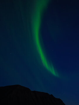 Aerial view of vibrant green aurora borealis dancing above the dark silhouette of a mountain range in Flateyri, Isafjardarbaer, Iceland.