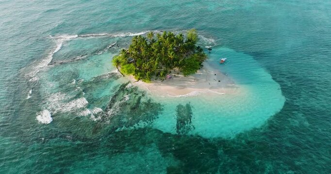 Aerial view of Guyam Island with lush palm trees and white sand beach surrounded by turquoise coral reef waters in General Luna, Caraga, Philippines.