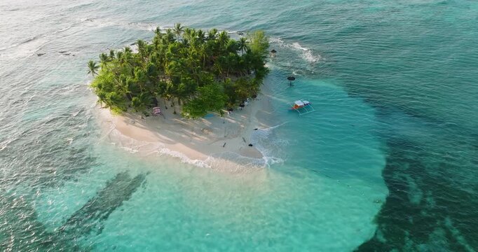 Aerial view of Guyam Island with lush palm trees and white sand beach surrounded by turquoise water in General Luna, Caraga, Philippines.