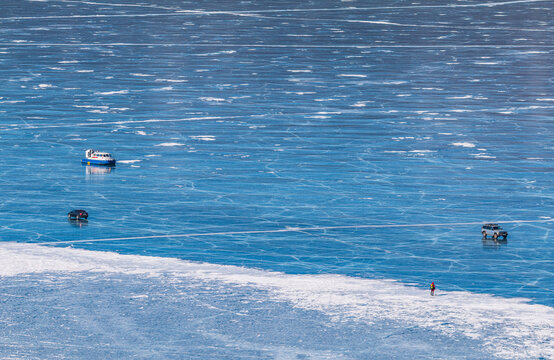 Aerial view of the frozen surface of Lake Baikal with a hovercraft, vehicles, and a person walking on the ice in Khuzhir, Irkutsk Oblast, Russia.