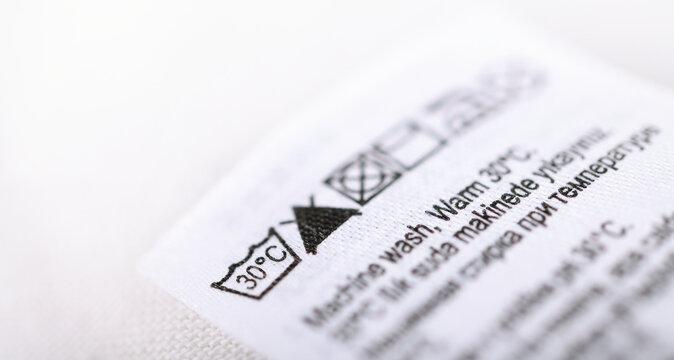 Close up of clothing care label with washing symbols on white fabric.