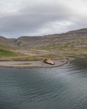 Aerial view of the historic Gardar BA 64 shipwreck resting on a remote beach surrounded by rugged mountains and calm coastal waters in Saudlauksdalur, Vesturbyggd, Iceland.