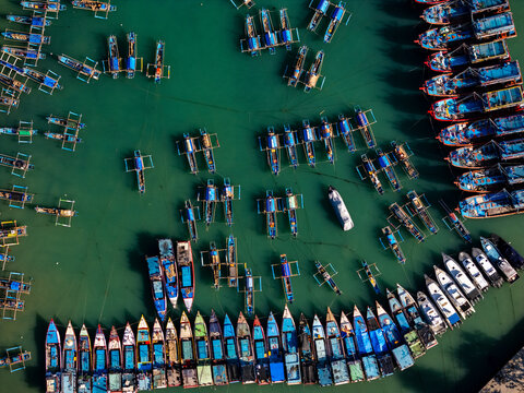 Aerial view of Pantai Sadeng with numerous colorful fishing boats moored in orderly rows in the turquoise waters of the harbor in Girisubo, Yogyakarta, Indonesia.