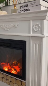 Close up slow motion camera movement towards modern white electric fireplace mantel with burning flames and decorative wood logs in cozy home