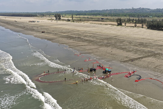 Cox's Bazar, Bangladesh - 10 April 2026: Aerial view of Cox's Bazar Sea Beach with fishermen using a tractor to pull large red fishing nets from the surf onto the sandy shore.