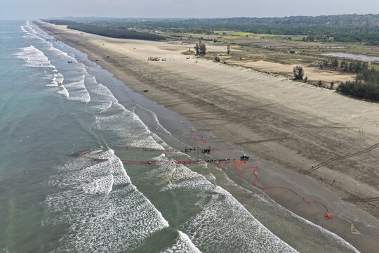 Cox's Bazar, Bangladesh - 10 April 2026: Aerial view of Cox's Bazar Sea Beach with fishermen pulling long red fishing nets from the surf onto the sandy shore.