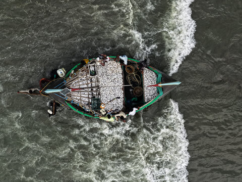 Cox's Bazar, Chittagong Division, Bangladesh - 10 April 2026: Aerial view of a wooden fishing boat filled with a large catch of fish, with fishermen working on deck.