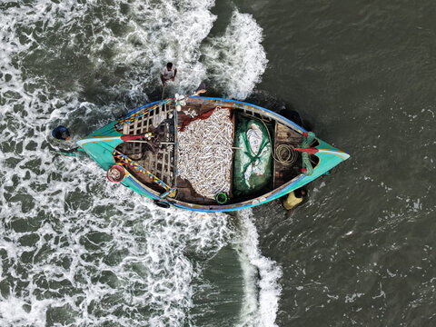 Cox's Bazar, Bangladesh - 10 April 2026: Aerial view of a traditional fishing boat filled with a fresh catch of fish, with fishermen working on board amidst the churning sea waves.
