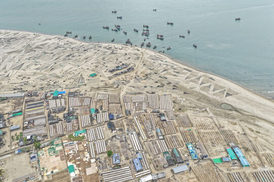Cox's Bazar, Bangladesh - 09 April 2026: Aerial view of Cox's Bazar with drying fish on the beach, small fishing boats in the sea, and rows of fish processing structures.