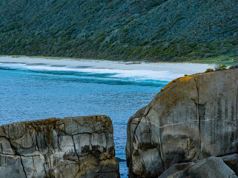 Aerial view of Shelly Beach with large granite rock formations, turquoise ocean waves crashing on the sandy shore, and coastal vegetation in West Cape Howe, Western Australia, Australia.
