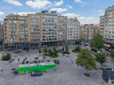 Ixelles, Bruxelles, Belgium - 03 July 2026: Aerial view of Place Eugene Flagey with historic buildings, trees, and pedestrians on the paved square under a blue sky.