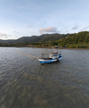 Aerial view of a traditional fishing boat anchored in the calm waters near Lanta Old Town, with lush green hills and a coastal landscape in the background Ko Lanta Yai, Krabi, Thailand.