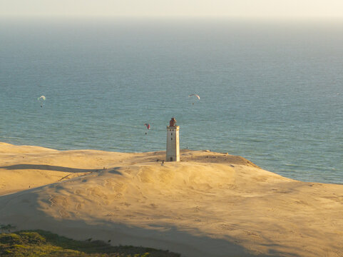 Aerial view of Rubjerg Knude lighthouse standing on sand dunes by the sea with paragliders in the sky in Lokken, Denmark.