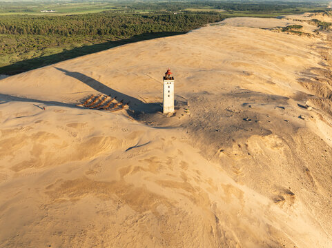 Aerial view of Rubjerg Knude lighthouse standing amidst vast sand dunes with long shadows cast across the landscape in Lokken, Denmark.