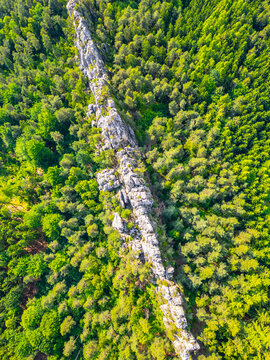 Aerial view of Suche skaly, a prominent sandstone rock formation rising above a dense green forest, captured from a high angle in Koberovy, Liberec Region, Czechia.