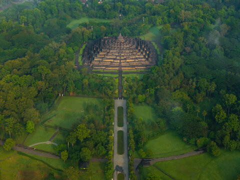 Aerial view of the ancient Borobudur Temple surrounded by lush green trees and tropical vegetation in the morning light in Kecamatan Borobudur, Jawa Tengah, Indonesia.