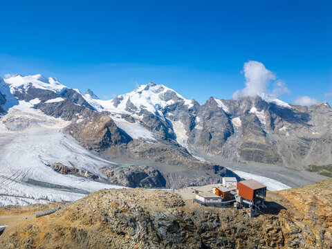 Aerial view of the Diavolezza hut nestled in the rugged Bernina Range with snow-capped peaks and a glacier in the background near Pontresina, Grisons, Switzerland.