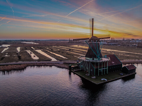 Aerial view of Zaanse Schans windmills standing by the water at sunset with golden light reflecting on the landscape in Zaandam, Noord-Holland, Netherlands.