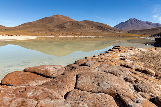 View of the red volcanic rock formations at Piedras Rojas reflecting in the calm waters of the lagoon under a clear blue sky in San Pedro de Atacama, Antofagasta, Chile.
