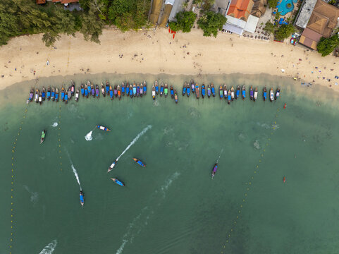 Aerial view of Railay Beach with numerous traditional long-tail boats moored along the sandy shore and turquoise water in Ao Nang, Krabi, Thailand.