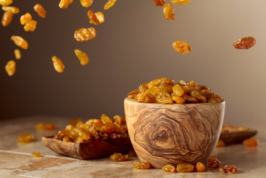 Yellow sultana raisins pour into a wooden bowl.
