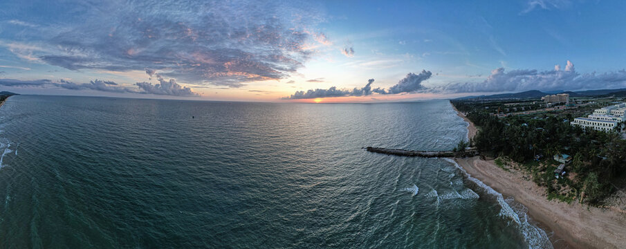 Aerial view of Long Beach at sunset with calm waters, a stone breakwater, and coastal buildings along the shore in Phu Quoc, Kien Giang, Vietnam.