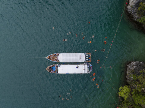 Aerial view of two tour boats anchored in the turquoise waters of Pi Leh Bay with people swimming nearby in Tambon Ao Nang, Chang Wat Krabi, Thailand.
