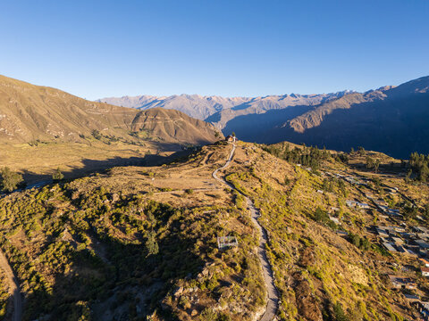 Aerial view of Colca Canyon featuring a winding path leading to a small structure on a hill, surrounded by rugged mountains and dry vegetation in Cabanaconde, Arequipa, Peru.