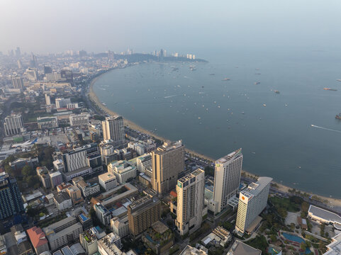 Aerial view of the Pattaya City skyline with high-rise hotels, a curved sandy beach, and boats anchored in the bay in Pattaya City, Chon Buri, Thailand.