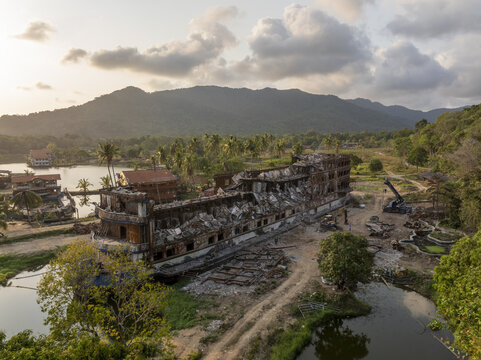Aerial view of the derelict ship-shaped building at Koh Chang surrounded by lush tropical vegetation, palm trees, and calm water in Trat, Thailand.