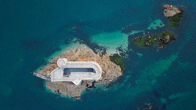 Aerial view of the historic fortress Chateau du Taureau on a rocky island surrounded by turquoise and deep blue sea water, Plouezoc'h, Bretagne, France.