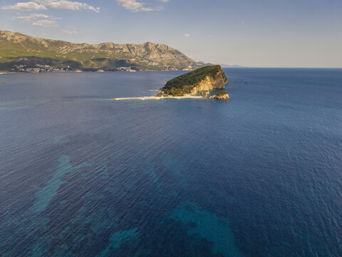 Aerial view of Sveti Nikola Island surrounded by the deep blue Adriatic Sea with the coastal mountains of Budva in the background Budva, Budva Municipality, Montenegro.