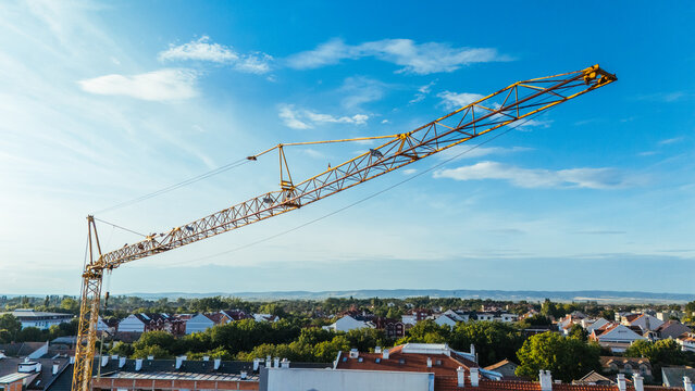 Aerial view of a yellow construction crane towering over a residential area with red-tiled roofs and lush green trees in Sremska Mitrovica, Vojvodina, Serbia.