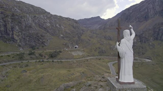 Aerial view of a white statue of Christ overlooking a winding mountain road and tunnel entrance in the Andes near Chavin de Huantar, Ancash, Peru.