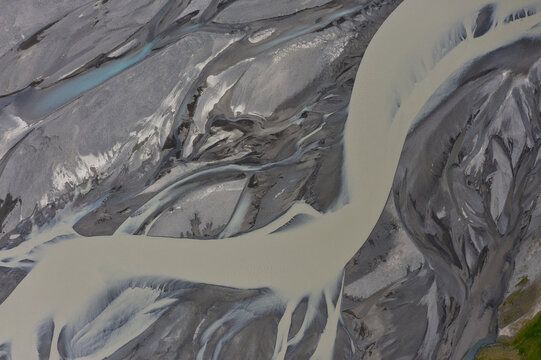 11 August 2021: Aerial view of braided river channels with sediment-rich water flowing through a grey gravel landscape.