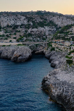 Aerial view of Ponte Ciolo spanning the rocky gorge with the deep blue sea below and coastal cliffs in Gagliano del Capo, Puglia, Italy.