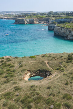Aerial view of Grotta Sfondata, a natural sinkhole with turquoise water surrounded by coastal cliffs and the Adriatic Sea, Otranto, Puglia, Italy.