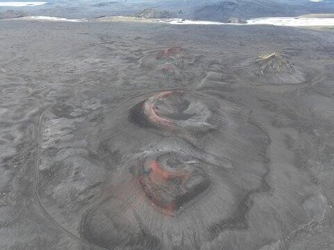 Aerial view of the volcanic craters of Blahylur in the highlands, featuring dark basaltic sand, reddish volcanic soil, and rugged terrain in Hella, Rangarthing ytra, Iceland.