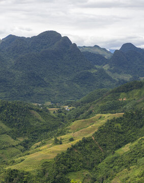 View of Ha Giang Loop featuring lush green mountains and terraced rice fields under a cloudy sky in Dong Van, Tuyen Quang, Vietnam.