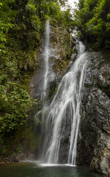 View of a cascading waterfall surrounded by lush green foliage and dark wet rocks along the Ha Giang Loop in Dong Van, Tuyen Quang, Vietnam.