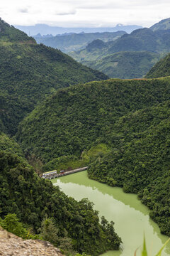 View of the Ha Giang Loop landscape with a river winding through lush green mountains and a small dam structure in Dong Van, Tuyen Quang, Vietnam.