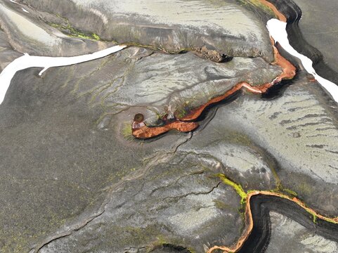 Aerial view of the volcanic landscape of Raudufossafjoll with red mineral deposits, dark basaltic soil, and green moss in Hella, Rangarthing ytra, Iceland.