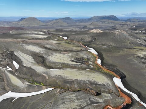 Aerial view of the volcanic landscape of Raudufossafjoll with patches of snow, mossy terrain, and a winding river in Hella, Rangarthing ytra, Iceland.