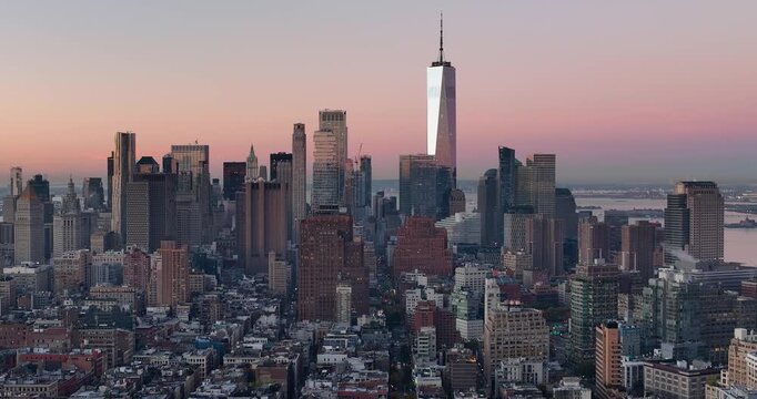 Aerial view of One World Trade Center rising above the Manhattan skyline during a soft sunset with glowing light on the glass facades in New York, New York, United States.