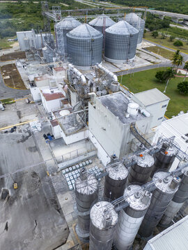 Aerial view of an industrial grain processing facility featuring large metal silos, complex piping systems, and storage buildings in Merida, Yucatan, Mexico.