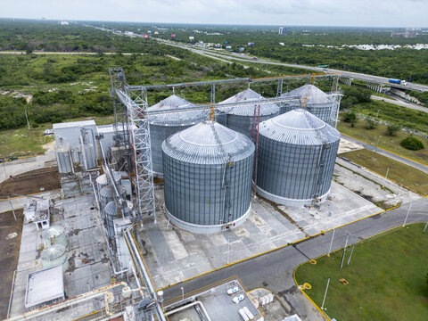 Aerial view of a large industrial grain storage facility with multiple metal silos situated near a highway in Merida, Yucatan, Mexico.
