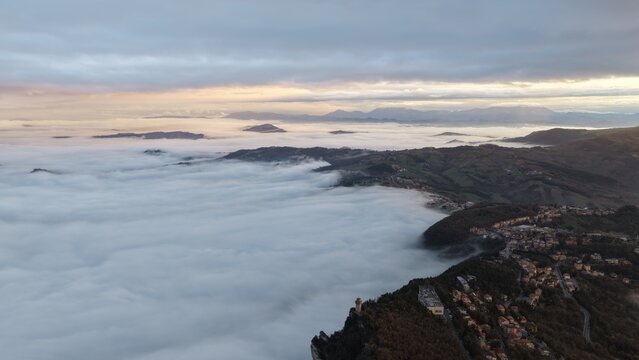 Aerial view of the historic city of San Marino perched on Mount Titano, surrounded by a thick sea of clouds at sunset, San Marino, San Marino, San Marino.