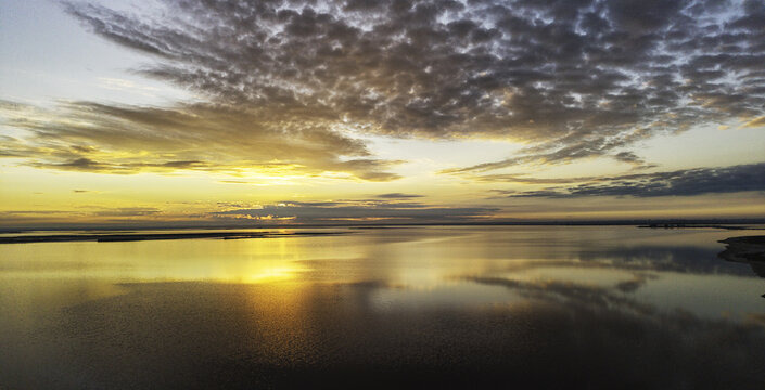 Aerial view of Lake Tyrrell at sunset with golden light reflecting on the calm water surface and textured clouds in the sky in Buloke Shire, Victoria, Australia.