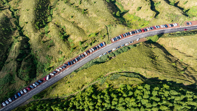 Aerial view of the road leading to Lagoa do Canario, lined with numerous parked cars amidst the lush green volcanic landscape in Santo Antonio, Azores, Portugal.